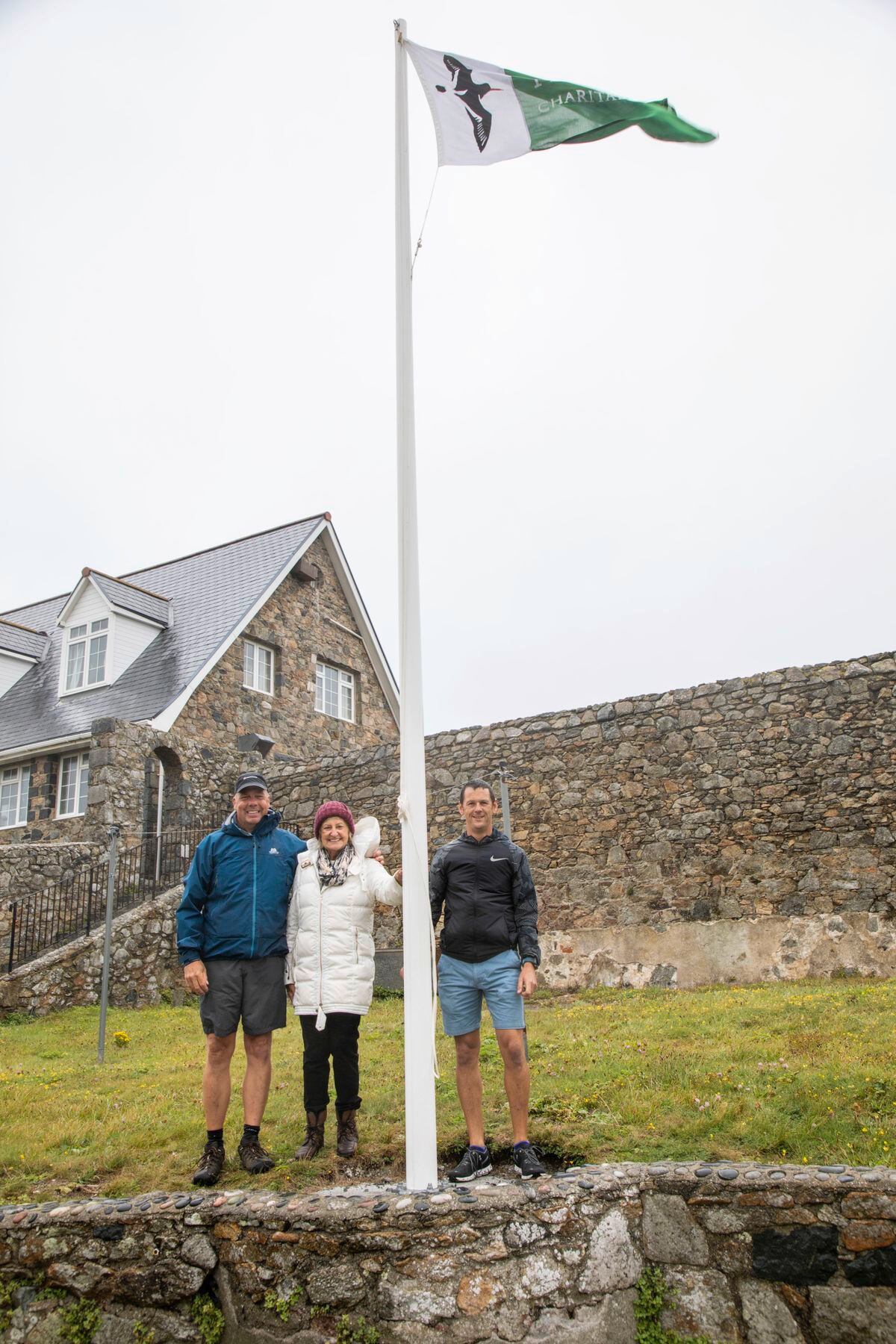 Lihou now has its own flag pole and flag, kindly donated to the island by Jean Rouget in honour of her late husband Mike. Left to right is former warden Richard Curtis, Jean Rouget and new Lihou warden Steve Sarre (Picture by Sophie Rabey, 25519959).