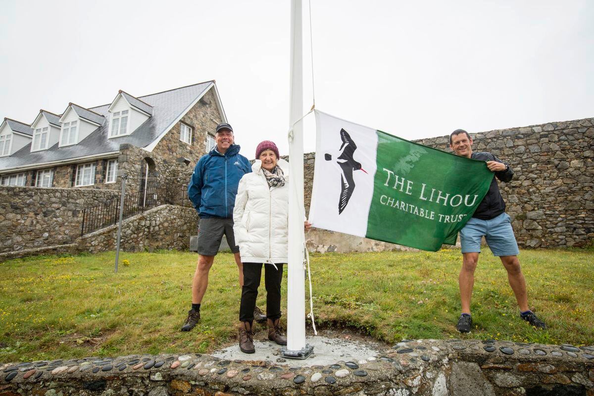 Lihou now has its own flag pole and flag, kindly donated to the island by Jean Rouget in honour of her late husband Mike. Warden Steve Sarre holds the flag and standing with Jean Rouget is former warden Richard Curtis (Picture by Sophie Rabey, 25519962).